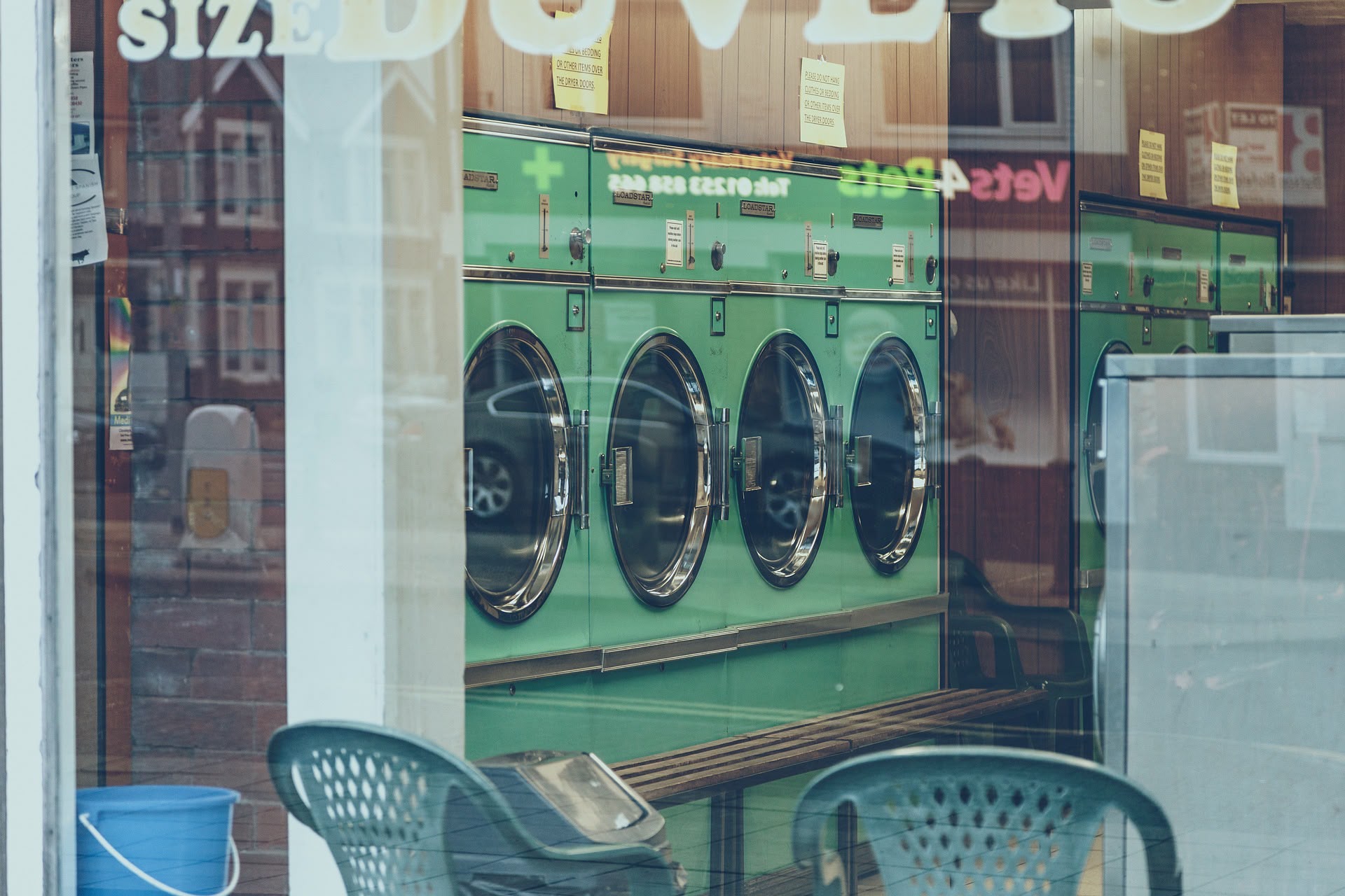 Blick durch das Schaufenster eines Waschsalons auf eine Reihe grüner Waschmaschinen.